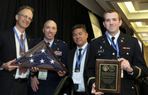 Left to right: David Zonies, MD, MPH; Jeremy W. Cannon, MD, FACS, Colonel, Medical Corps, AFRC; COL (Ret.) Robert B. Lim, MD, FACS; and 2LT Theodore McLean hold a plaque and flag honoring Basil A. Pruitt, Jr., MD, FACS, at the annual Excelsior Surgical Society meeting.